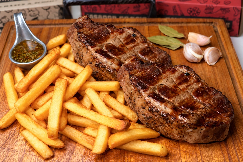 Brasero con dos porciones de carne asada, papas y salsa chimichurri